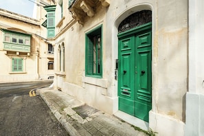 Straßenansicht eines Gebäudes mit grünen Türen und Fensterläden, einem Bürgersteig und einer Straße.