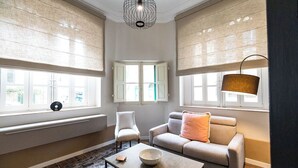 Ein Wohnzimmer mit Sofa, Sesseln, Couchtisch und einem Fenster mit Jalousien.