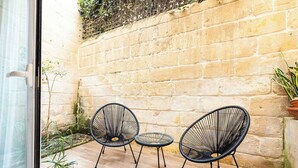 Ein kleiner Patio-Bereich mit zwei schwarzen Stühlen aus Draht und einem kleinen runden Tisch, einer Steinmauer und Topfpflanzen.