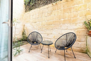 Ein kleiner Patio-Bereich mit zwei schwarzen Stühlen aus Draht und einem kleinen runden Tisch, einer Steinmauer und Topfpflanzen.