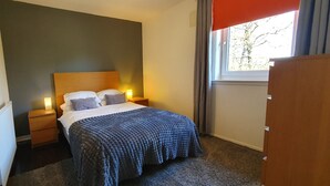 A bedroom with a bed, bedside lamps, a radiator, and a window with curtains. - 2BR- Modern, top floor apartment  -  Free parking fast internet.  Near hospitals (Aberdeen)