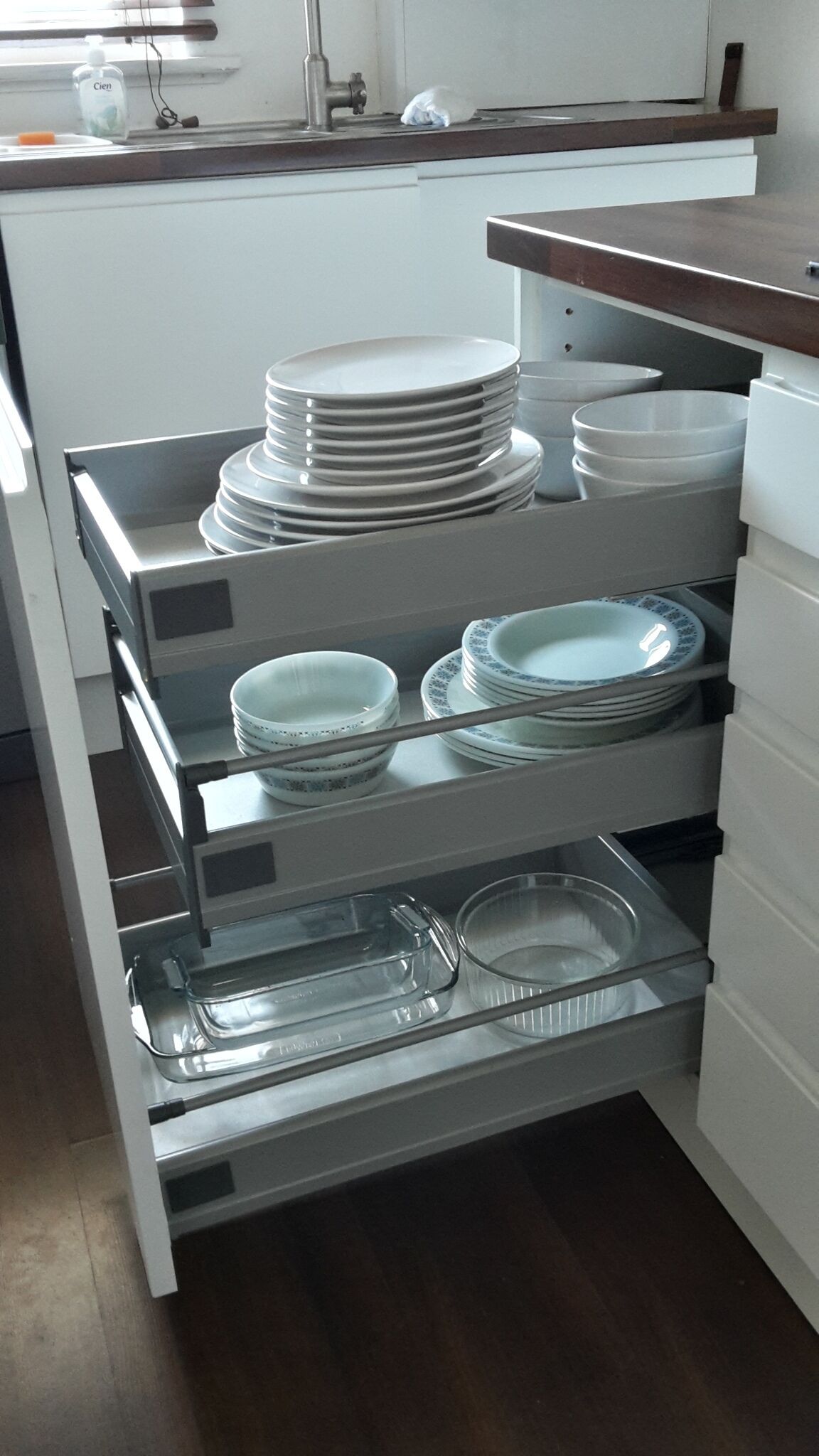 A kitchen with a built-in utensil drawer containing plates, bowls, and a glass container.