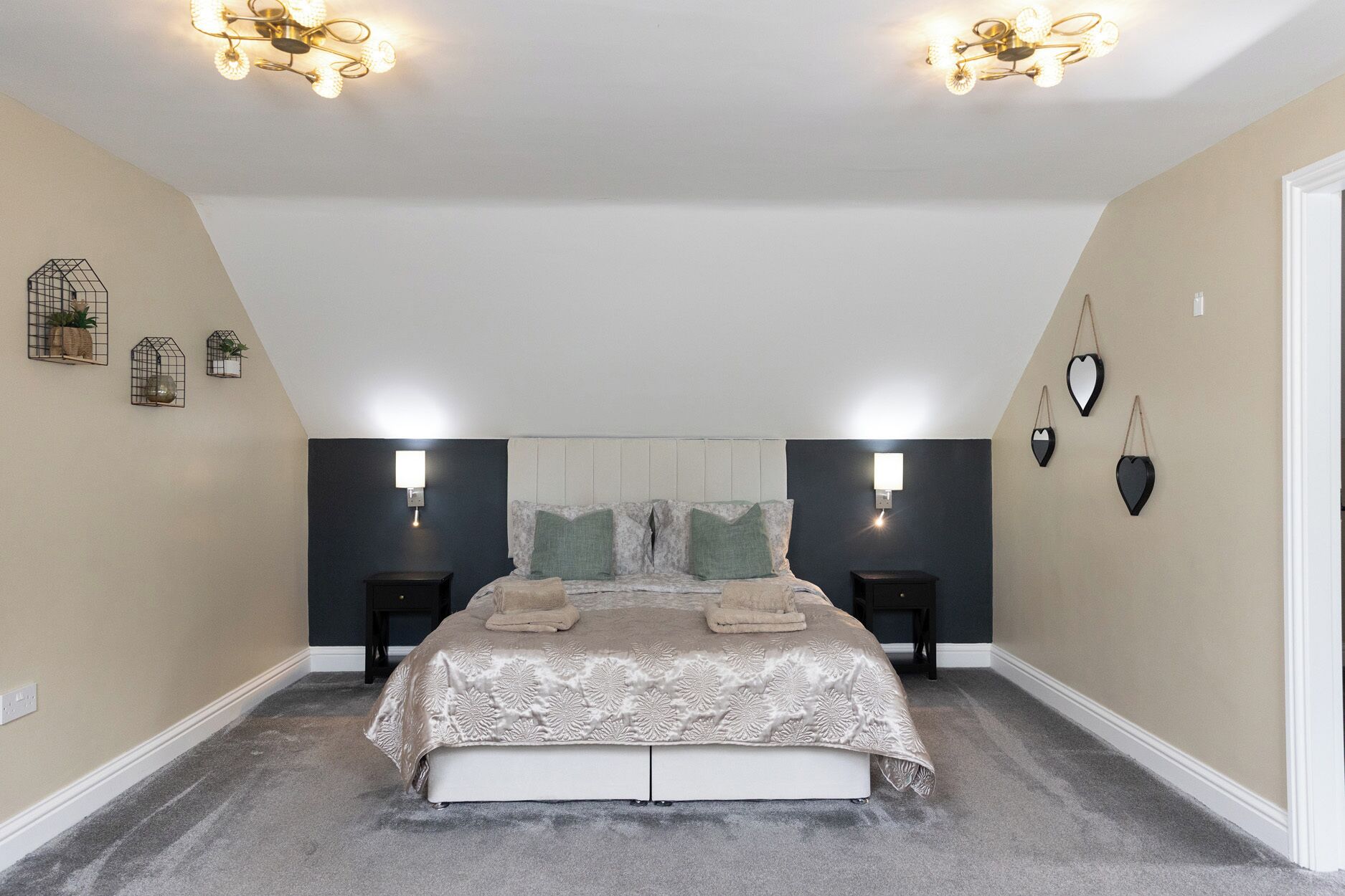 A bedroom with a bed, two bedside tables, a chandelier, wall sconces, and decorative wall art.