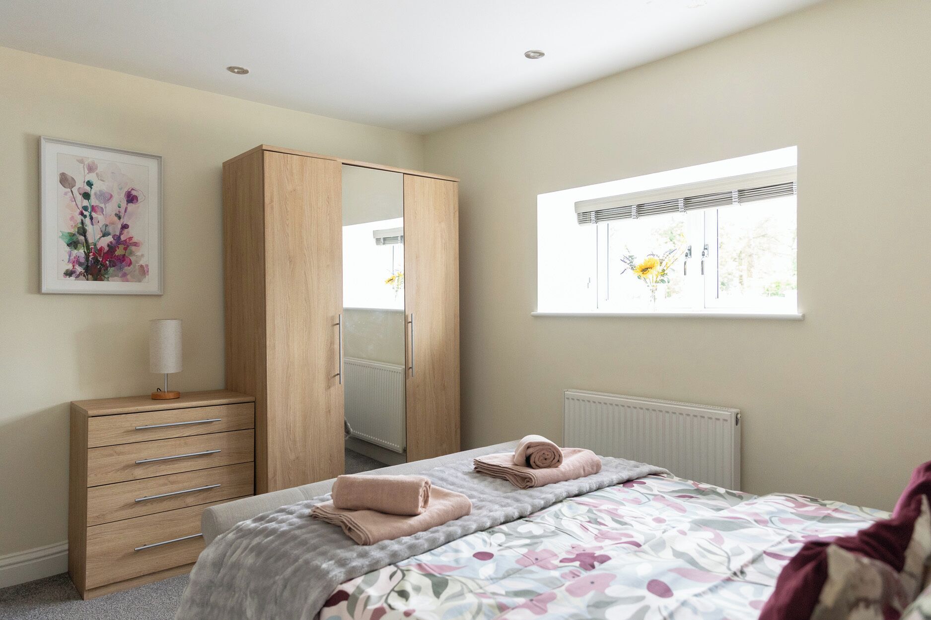 A bedroom with a bed, a dresser, a wardrobe, a radiator, a window with a view, and a framed picture on the wall.