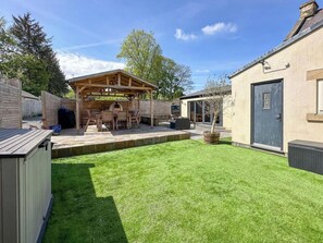 Ein Garten mit einer Holz-Pergola, einem Grillplatz und einer Tür.
