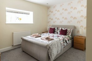 Une chambre à coucher comprenant un lit, une table de chevet, un radiateur, une fenêtre avec des stores et un mur orné d’un motif.