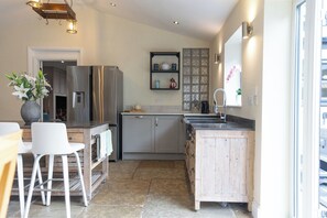 A kitchen with a refrigerator, sink, and bar stools. - The Old Sawmill (Newcastle-upon-Tyne)