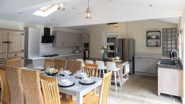 A spacious kitchen with high ceilings, modern appliances, and a dining area set for a meal. - The Old Sawmill (Newcastle-upon-Tyne)