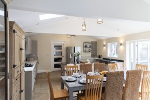 Un coin repas avec une table dressée pour six personnes, une cuisine en arrière-plan et une vue sur l’extérieur par le biais d’une grande fenêtre.