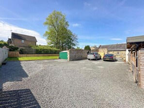A gravel driveway leading to a garage with two cars parked, surrounded by stone walls and a green shed. - The Old Sawmill (Newcastle-upon-Tyne)
