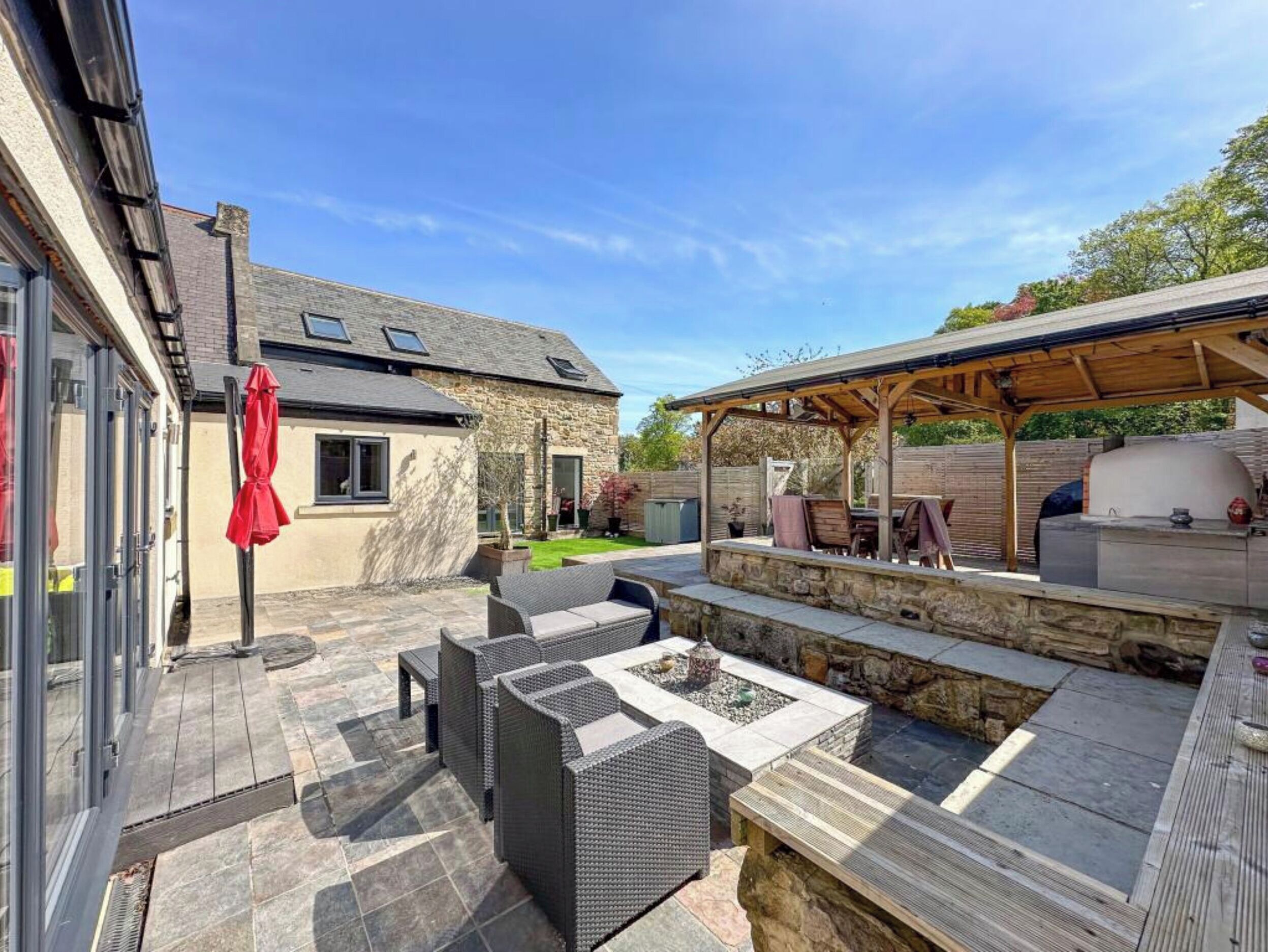 Un patio con mobiliario exterior, una parrilla y un edificio de piedra.