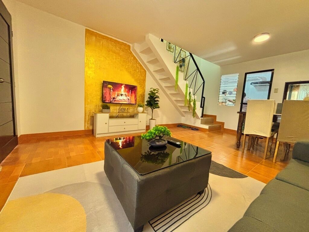 Una sala de estar moderna con una escalera, un televisor de pantalla plana, un sofá y una mesa de centro.