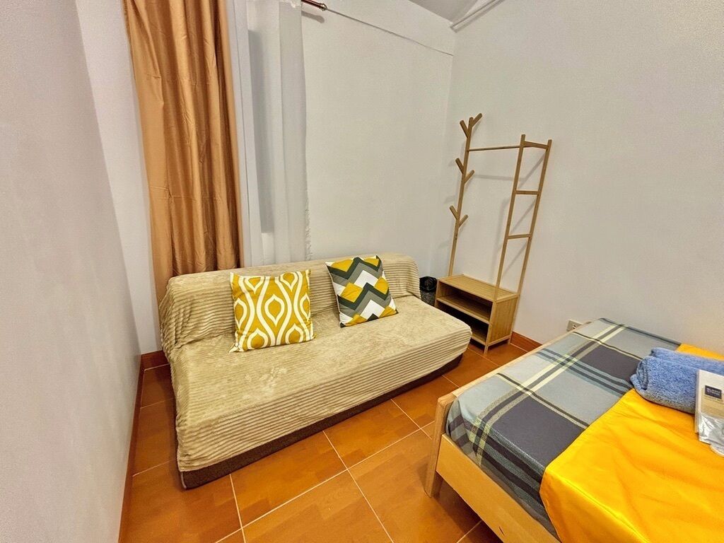 A small room with a sofa, a bed, a wooden ladder, and a shelf.