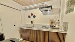 Eine kompakte Küche mit eingebauter Arbeitsplatte, einer Wand-Klimaanlage und einem kleinen Spülbecken.