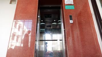 Un ascensor con un letrero que indica 'No se permite comida en la habitación' y un mensaje en otro idioma solicitando que entren menos personas a la vez.