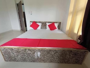 Una cama con colcha roja, dos almohadas y un cabecero con diseño texturizado.