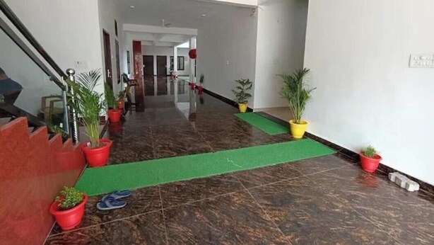 Un vestíbulo de hotel con piso de mármol, plantas en macetas, alfombra verde y una escalera.