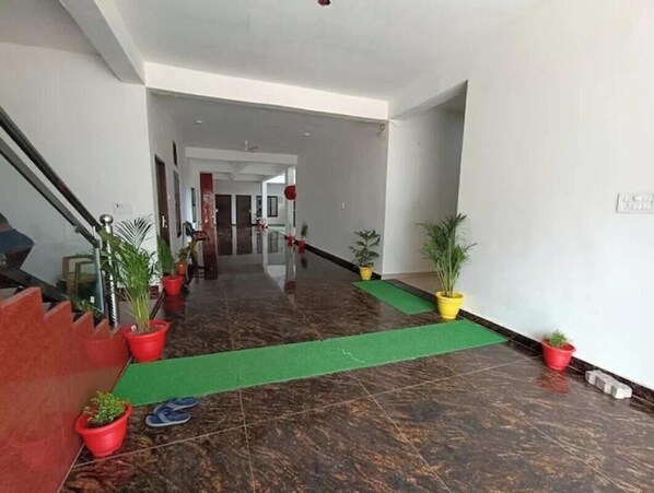 Un vestíbulo de hotel con piso de mármol, plantas en macetas, alfombra verde y una escalera.