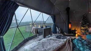 A cozy tent with a view of the outdoors, a table with candles, a small Christmas tree, and a fireplace. - Geodome with Hot Tub (Dorset)