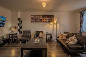 Ein modernes Wohnzimmer mit Sofa, Ohrensessel, Couchtisch und Kunstwerk an der Wand.