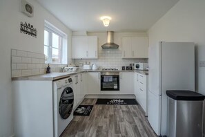 Eine kompakte Küche mit weißen Schränken, einem eingebauten Backofen, einer Mikrowelle und einem Edelstahlkühlschrank.