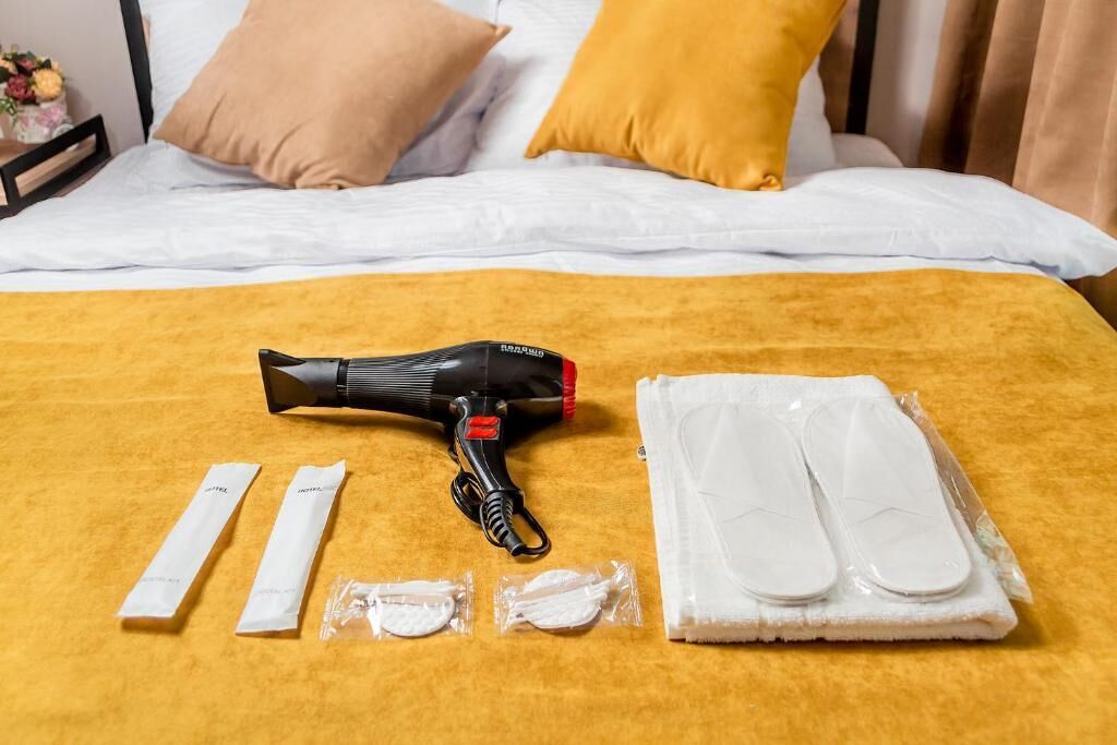 A bed with a yellow blanket, a black hairdryer, white slippers, and a white towel on a hotel room.