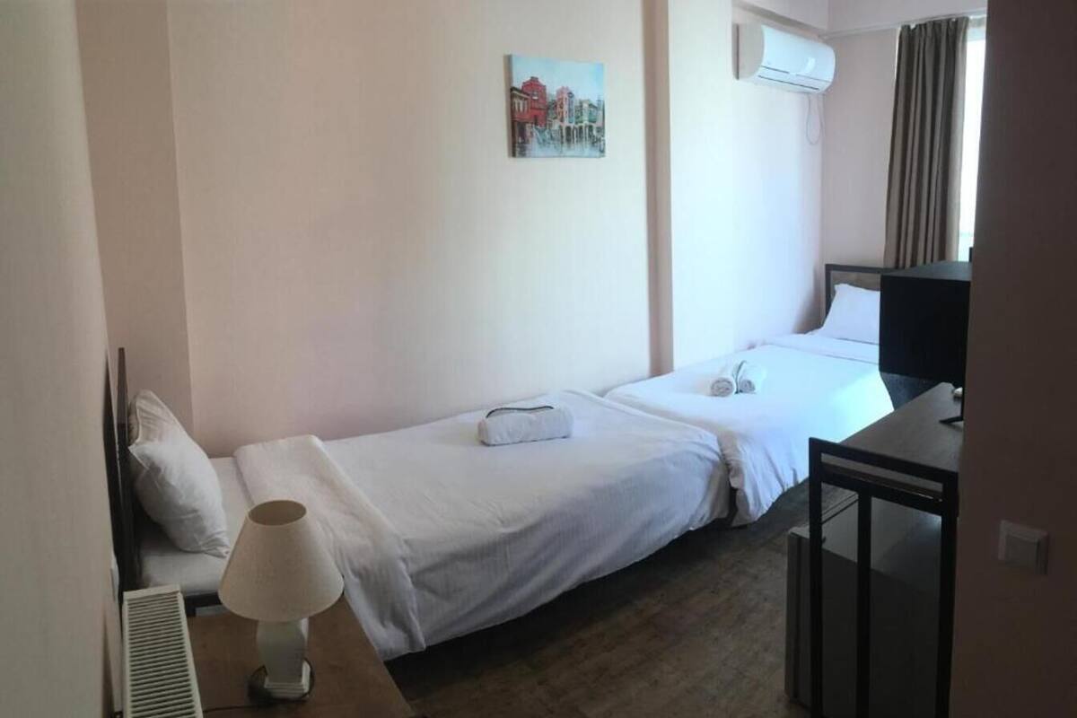 Habitación de hotel con dos camas, un escritorio, una lámpara, un equipo de aire acondicionado y un cuadro en la pared.