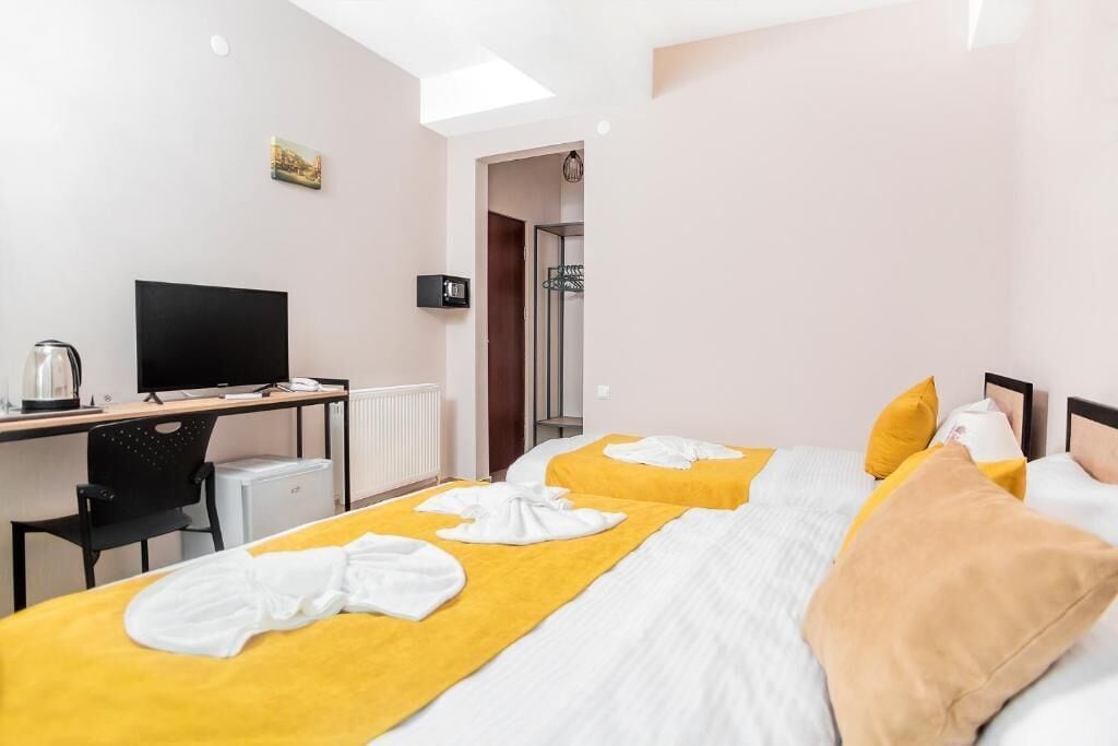 Quarto de hotel com duas camas, uma mesa de escritório com computador, televisão e chuveiro.