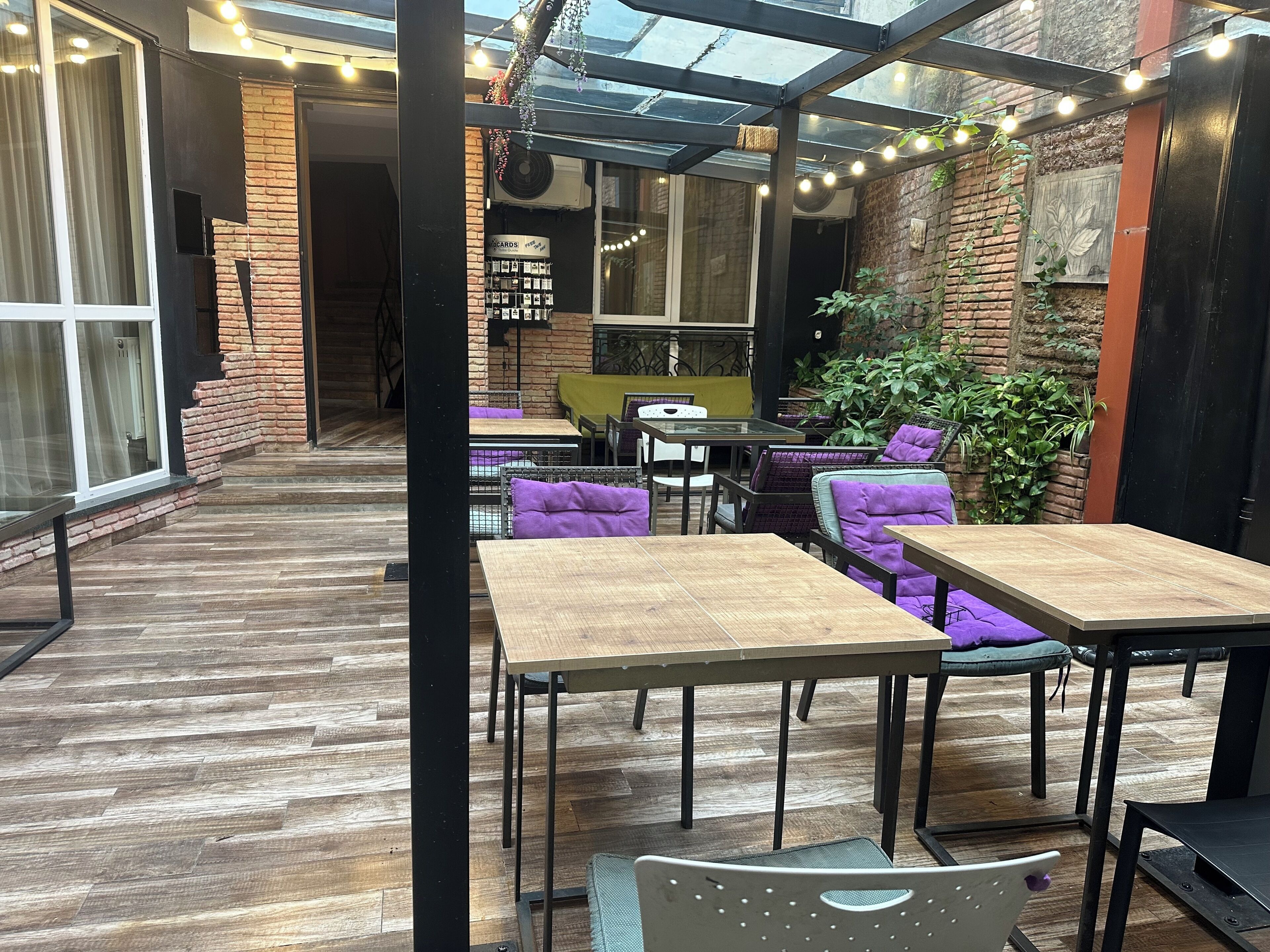 An indoor patio area with wooden flooring, tables, chairs, and a brick wall.