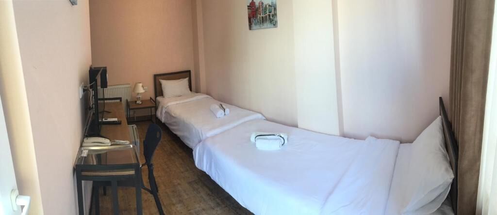 A single-bed room with a desk, chair, and a small table with a lamp.