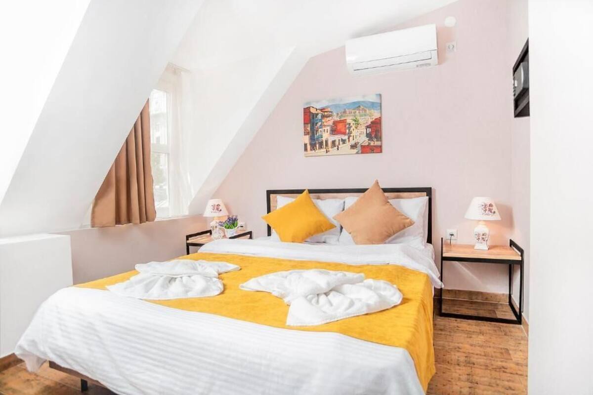Un dormitorio con una cama, un cuadro, una mesita de noche, una lámpara y una ventana con cortinas.