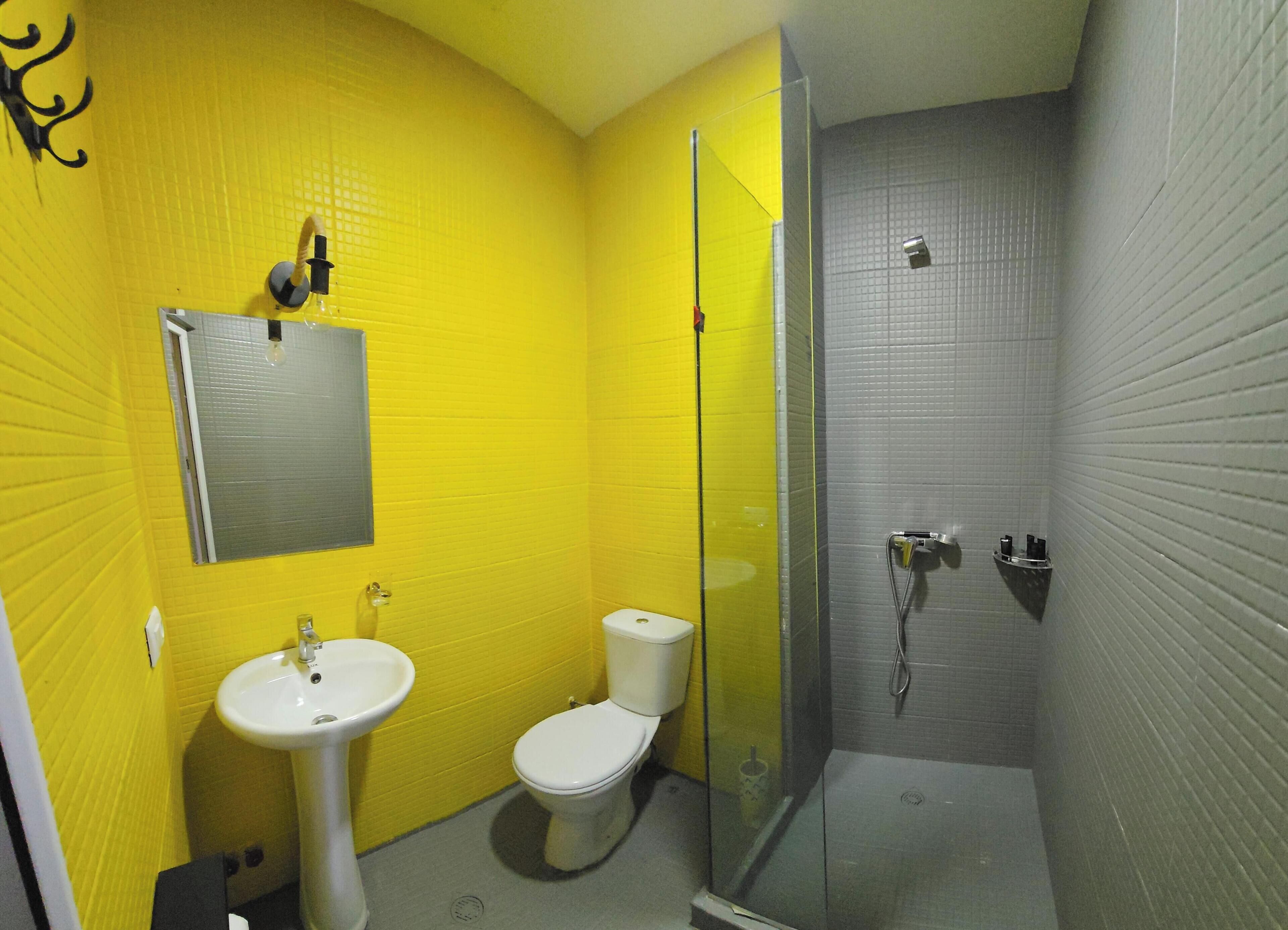 A bathroom with yellow walls, a white sink, a toilet, and a glass-enclosed shower area.