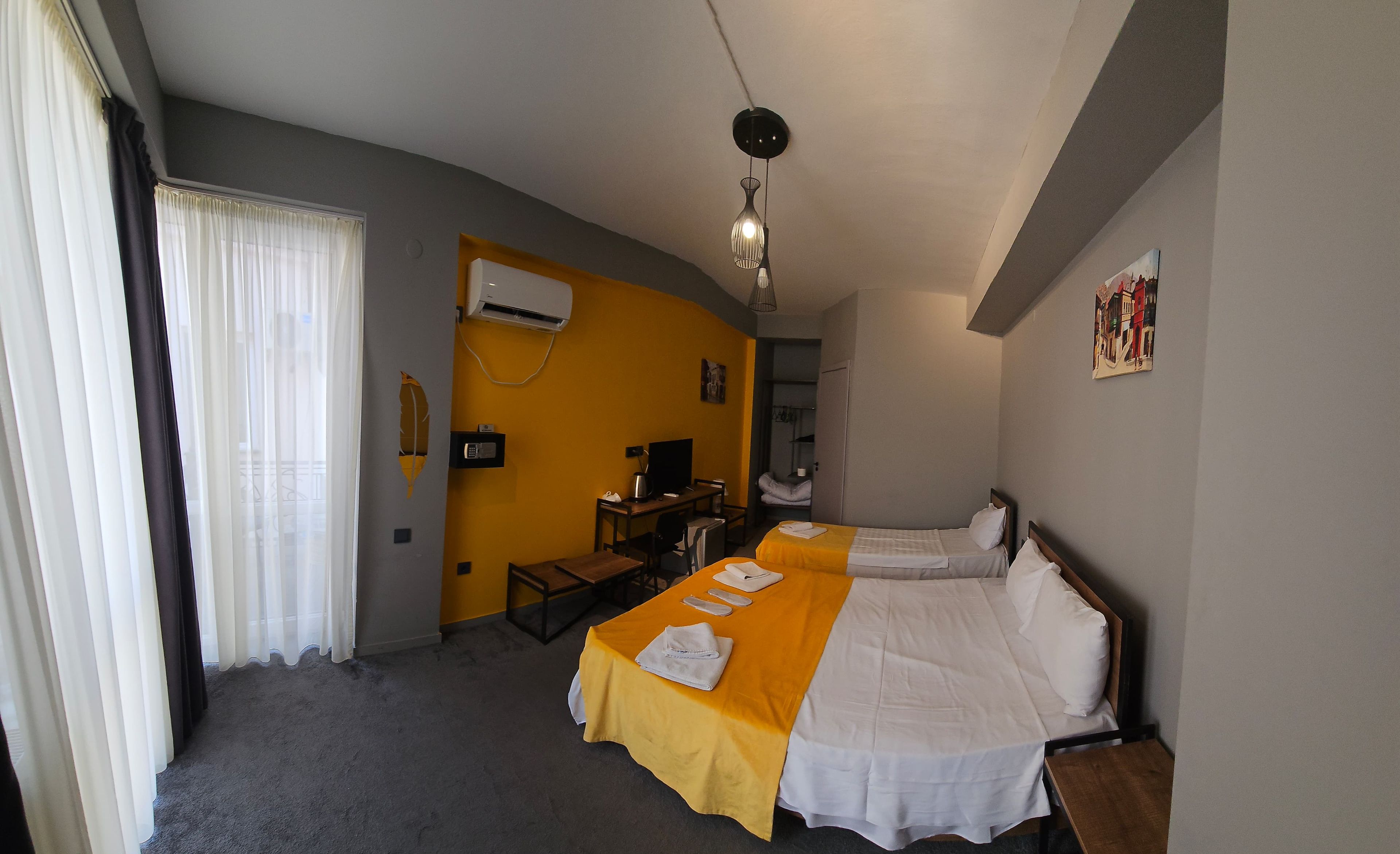 A hotel room with two beds, a desk, an air conditioning unit, and a painting on the wall.