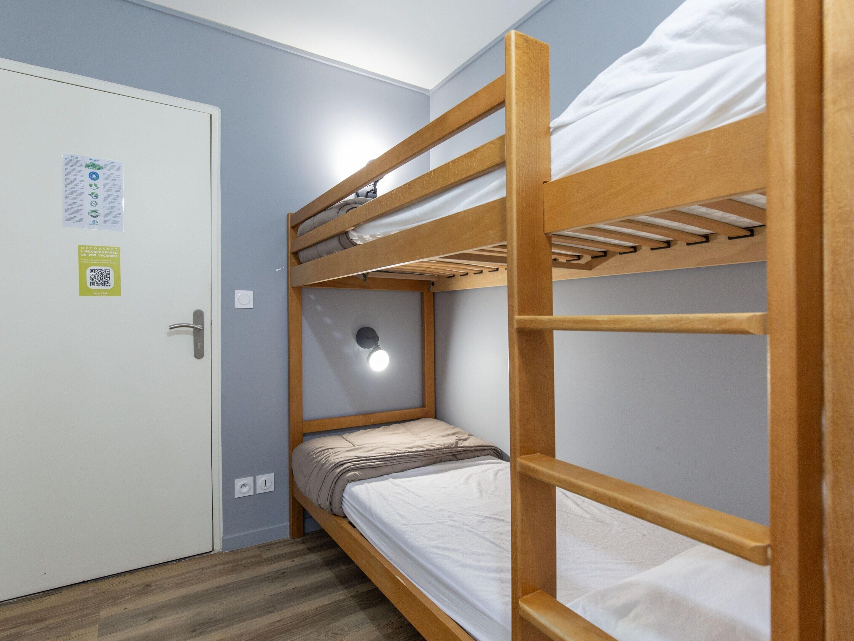 Habitación con literas, una puerta, un accesorio de iluminación y un código QR en la pared.
