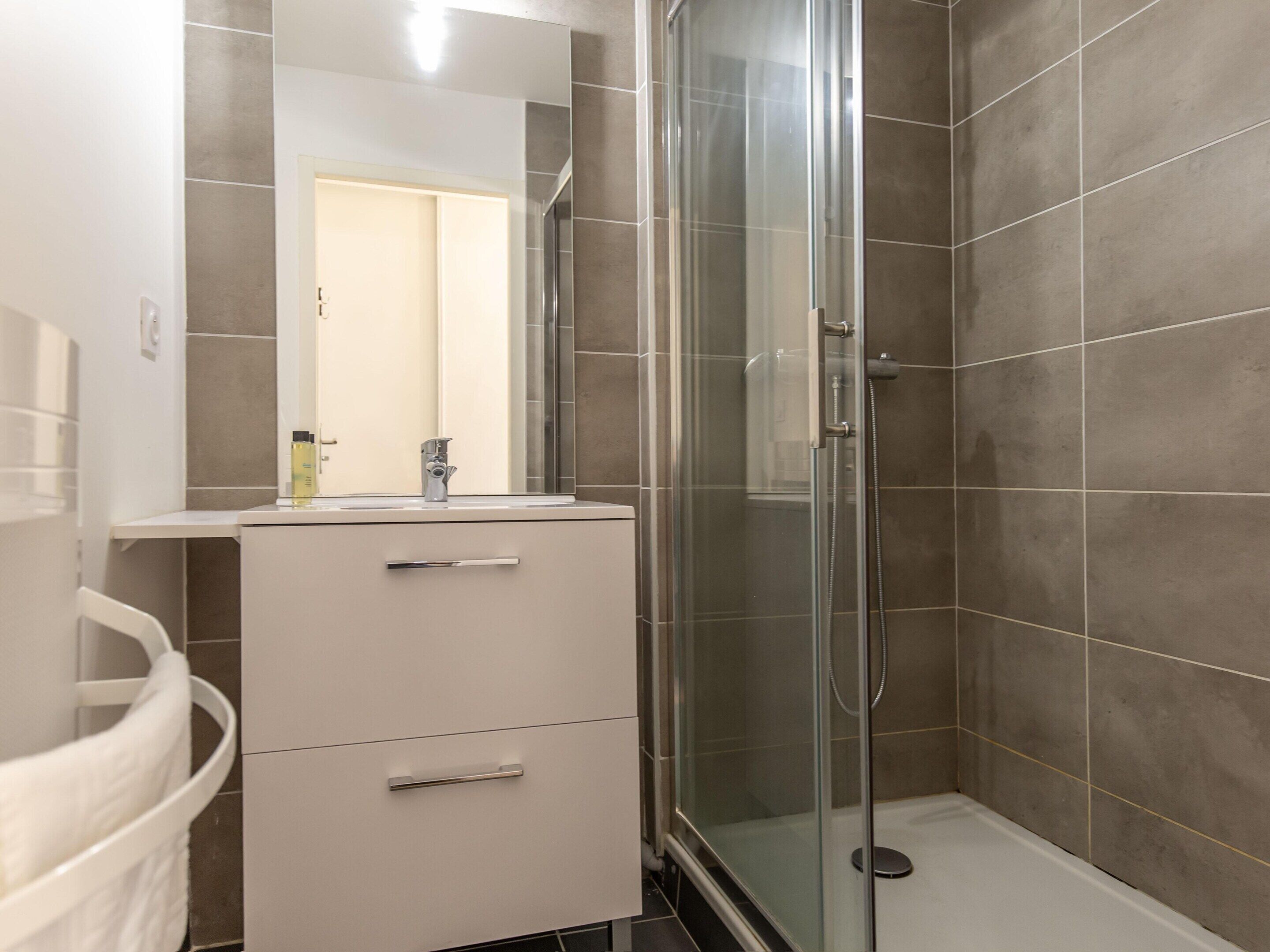 A bathroom with a glass-enclosed shower, a sink with a mirror, and a cabinet with drawers.