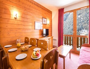 Ein Holzinterieur mit einem Esstisch, Stühlen, einem Fernseher und einem Balkon mit Blick auf Schnee.