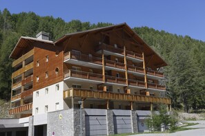 Ein mehrstöckiges Hotel mit Balkonen, einem Steinsockel und einem bewaldeten Hintergrund.