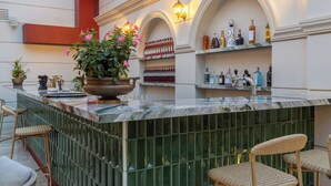 A bar area with a marble countertop, wicker bar stools, a potted plant, and a wine rack with bottles.