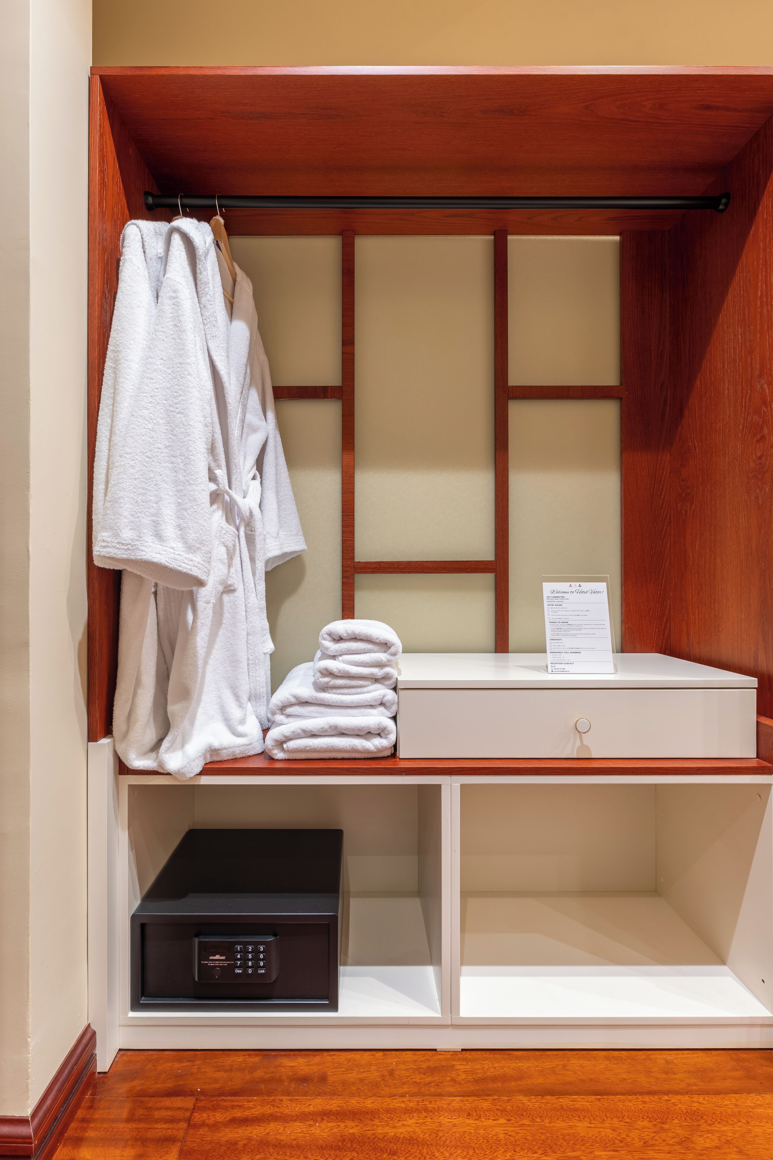 A wooden closet with a robe rack, folded towels, and a black electronic device.