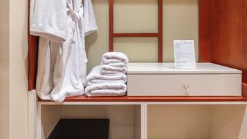 A wooden closet with a robe rack, folded towels, and a black electronic device.