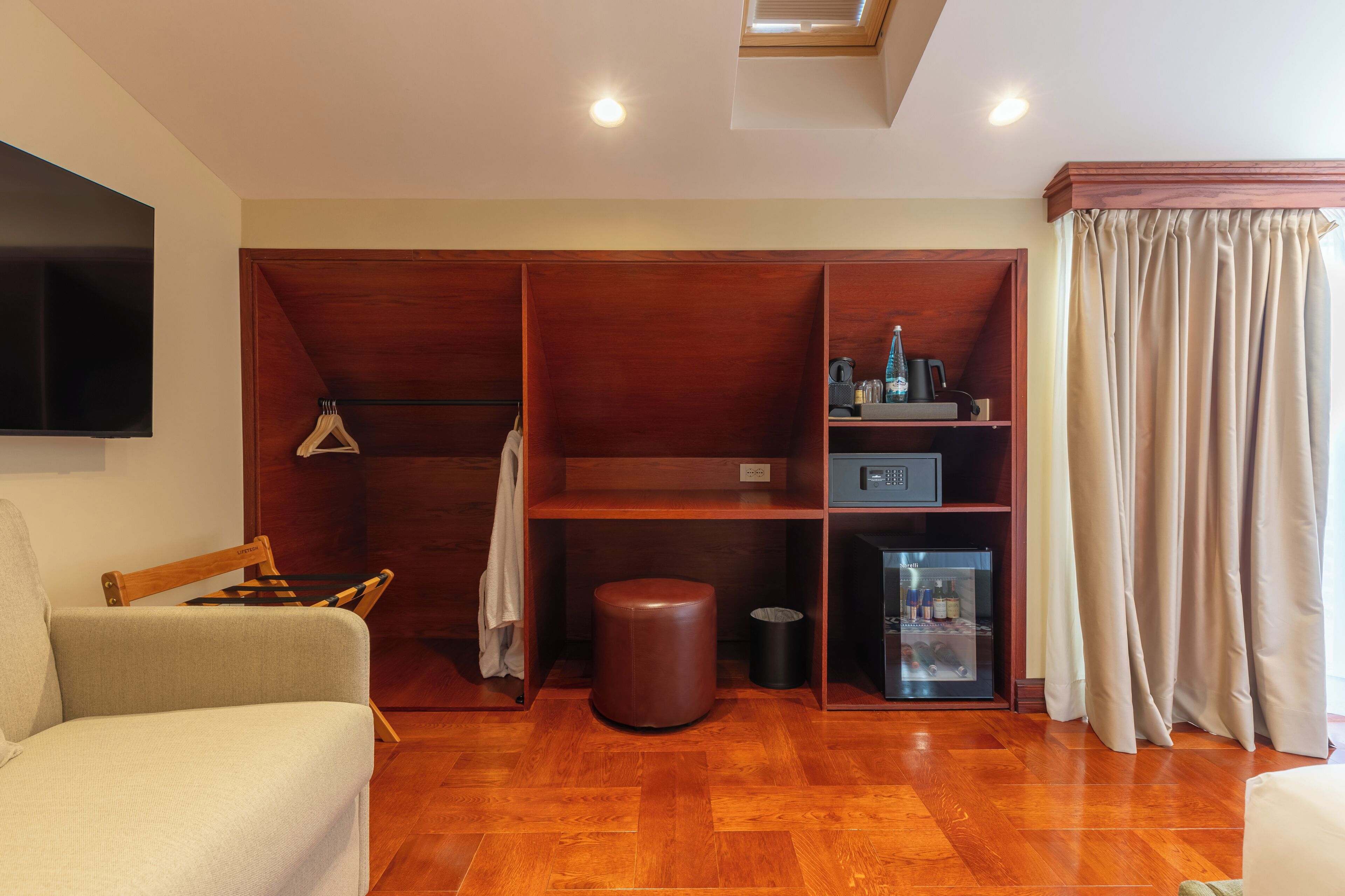 A room with a wooden floor, a sofa, a TV, a wardrobe, a small table, and a window with curtains.