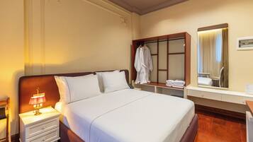 A hotel room with a large bed, a nightstand with a lamp, a mirror, and a robe hanging on a rack.