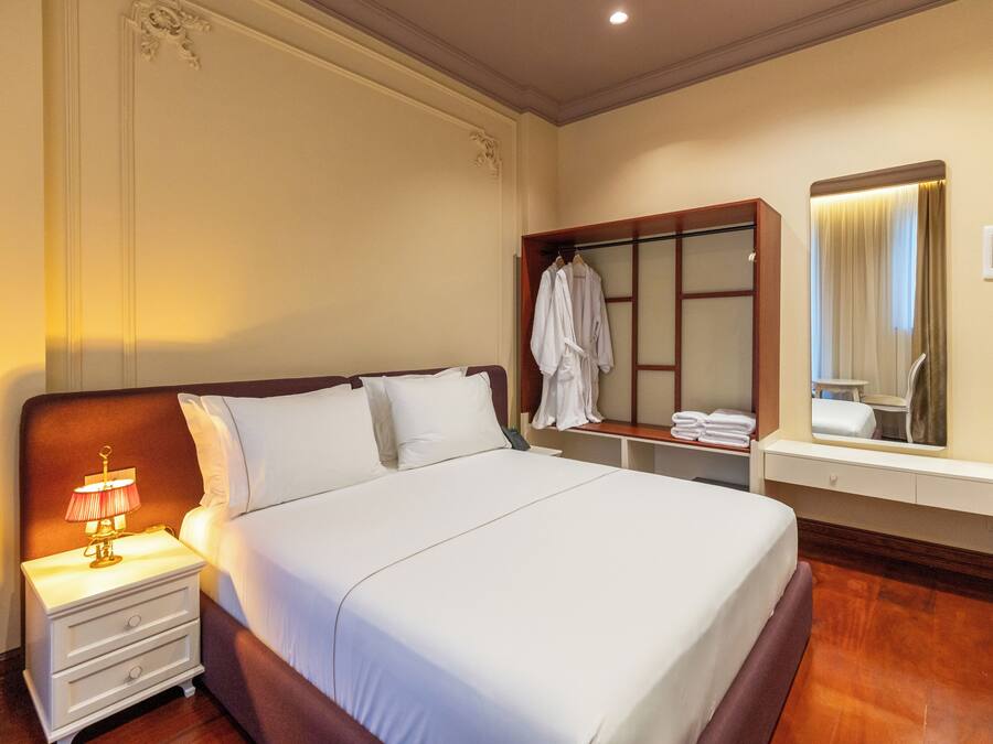 A hotel room with a large bed, a nightstand with a lamp, a mirror, and a robe hanging on a rack.