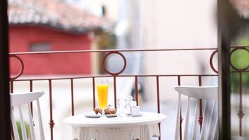 A balcony with a table and chairs, a glass of orange juice, and a red building in the background.