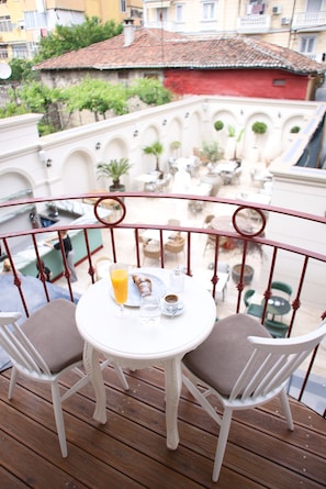 Un balcón con una mesa, sillas, un vaso de jugo de naranja y un croissant.