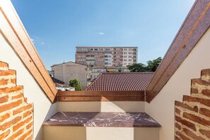 A view from a balcony with a tiled roof, brick walls, and a building in the background.