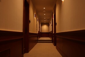 Un pasillo estrecho y tenuemente iluminado con paredes de madera y suelo alfombrado, que conduce a una escalera.