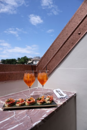 A terrace with a table set for two, glasses of a beverage, and a plate of appetizers. - Vatër Hotel (Shkodër)