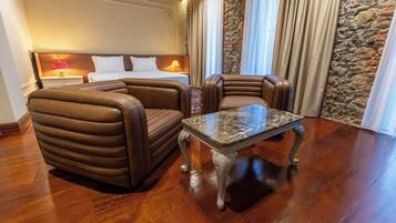 Una habitación de hotel con una cama, dos sillones de cuero, una mesa de centro de mármol, una mesita de noche con lámpara y una pared de acento de piedra.