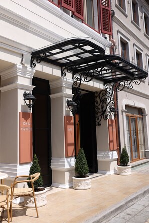 A building entrance with a covered porch, columns, and potted plants. - Vatër Hotel (Shkodër)